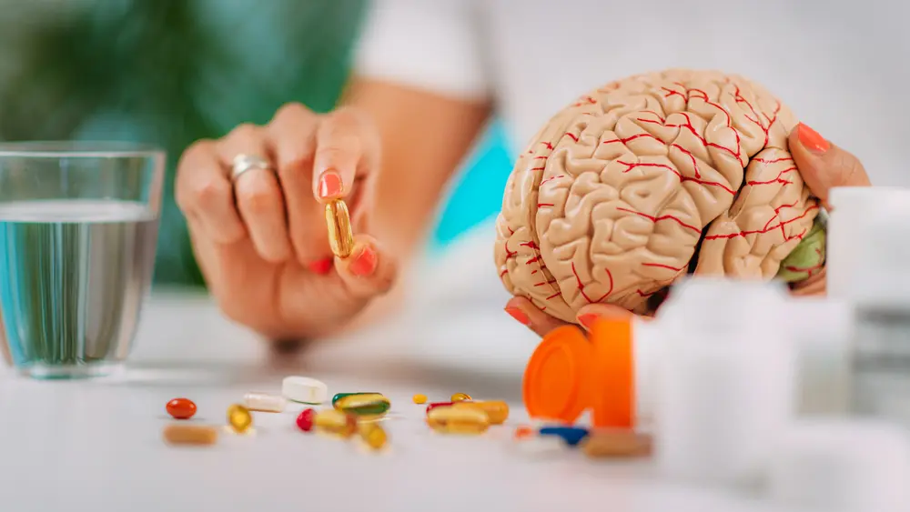 Woman holding a brain supplement capsule beside a model brain, representing cognitive improvement and brain health support.