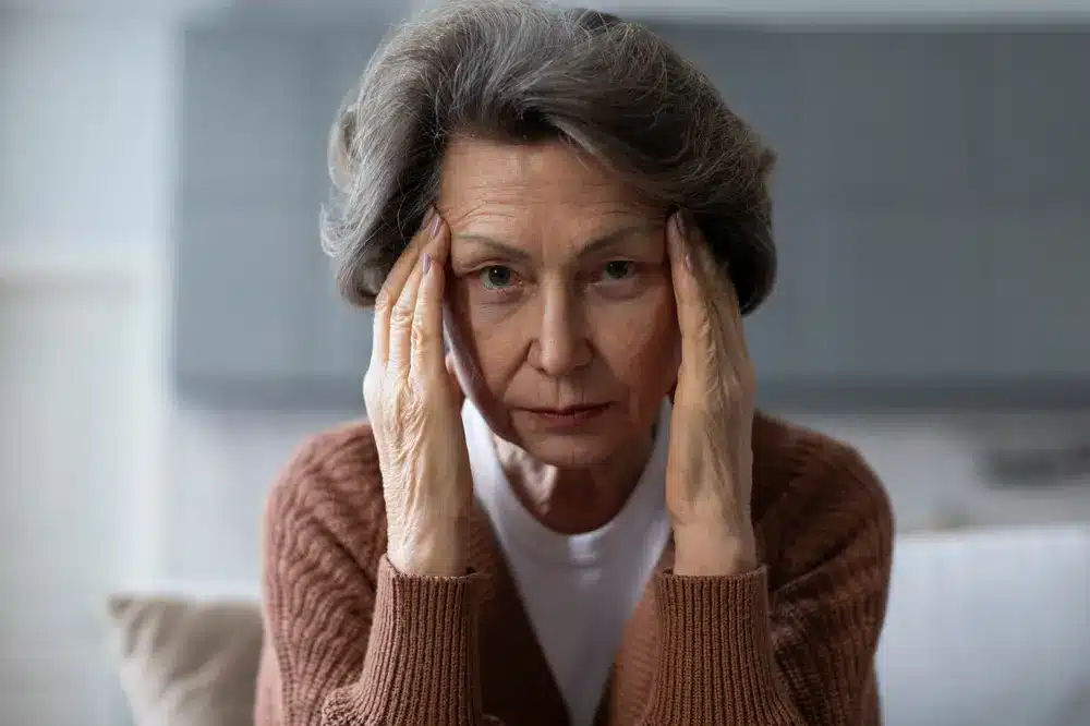 Sad elderly woman touching her temples, showing signs of anxiety, depression, or dementia related to aging.